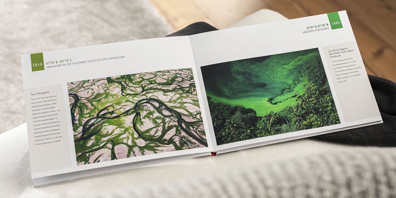 Ein geöffnetes Fotobuch zeigt zwei Seiten mit grünen Landschaftsbildern. Auf der linken Seite ist ein Bild mit vielen grünen Linien, auf der rechten Seite sieht man eine ruhige grüne Wasserfläche.
