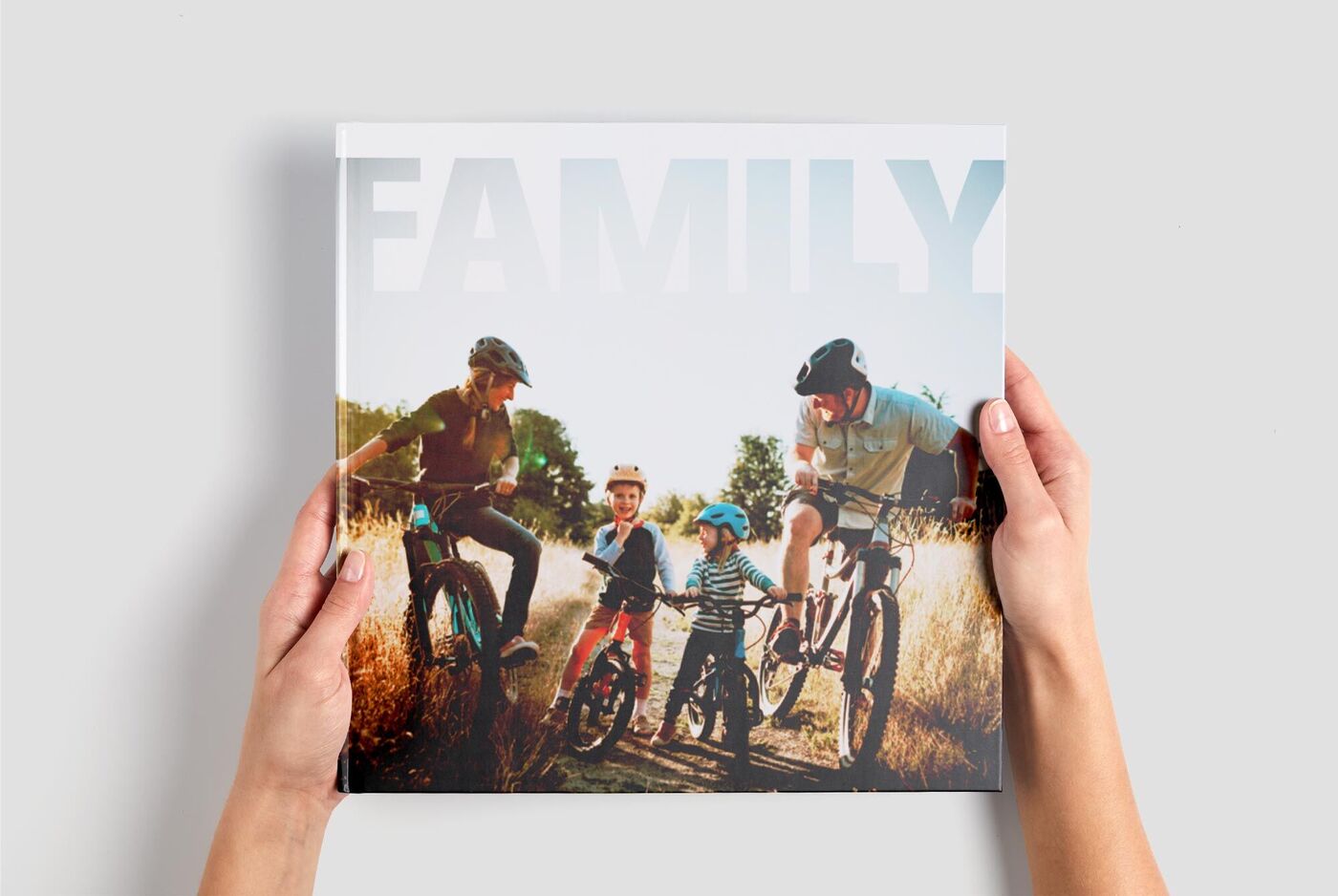 Eine Familie hält ein Fotobuch mit der Aufschrift "Family" in den Händen und genießt die Zeit im Freien