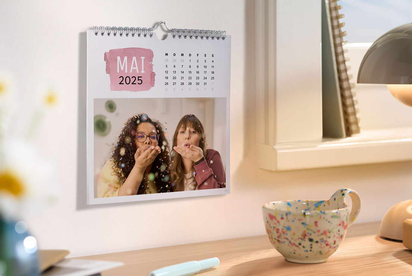 Ein Fotokalender zeigt den Monat Mai 2025 mit fröhlichen Personen, die Funken sprühen.