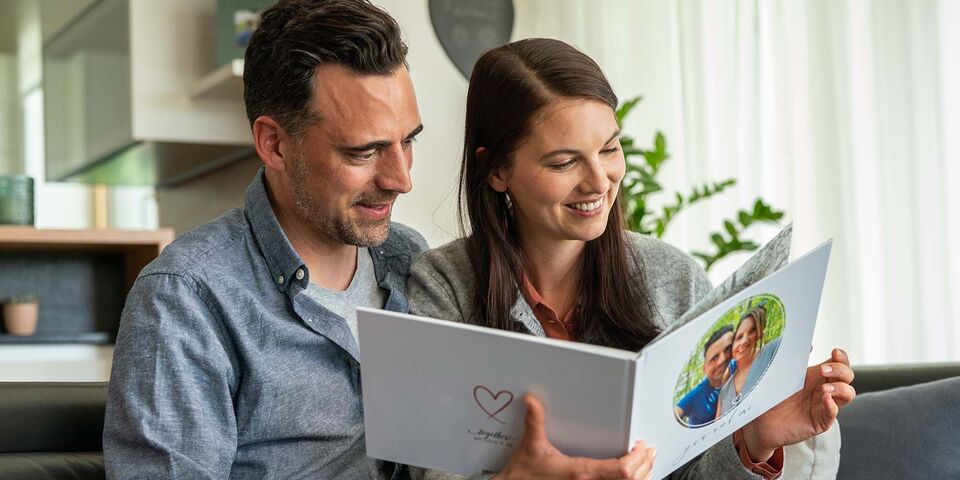 Paar schaut gemeinsam in ein CEWE Fotobuch mit persönlichen Erinnerungen.