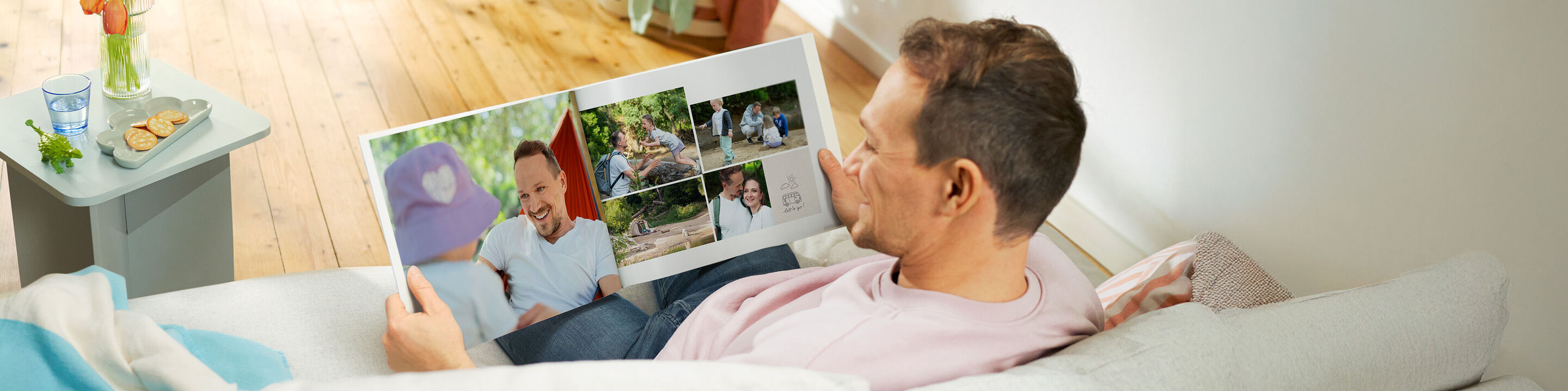 Eine Person betrachtet ein CEWE FOTOBUCH mit schönen Erinnerungen auf der Couch.