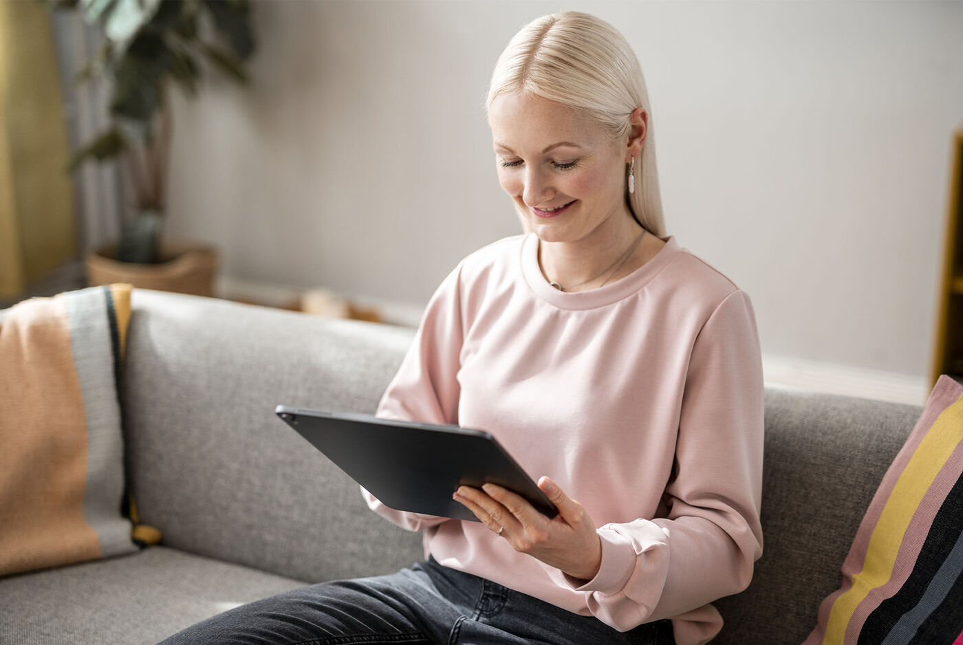 Person mit einem Tablet auf dem Sofa, umgeben von einer gemütlichen Atmosphäre