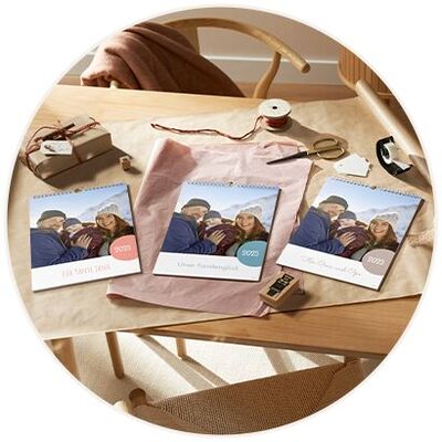 Drei liebevoll gestaltete CEWE Fotokalender liegen auf einem Tisch mit kreativen Materialien und Geschenken