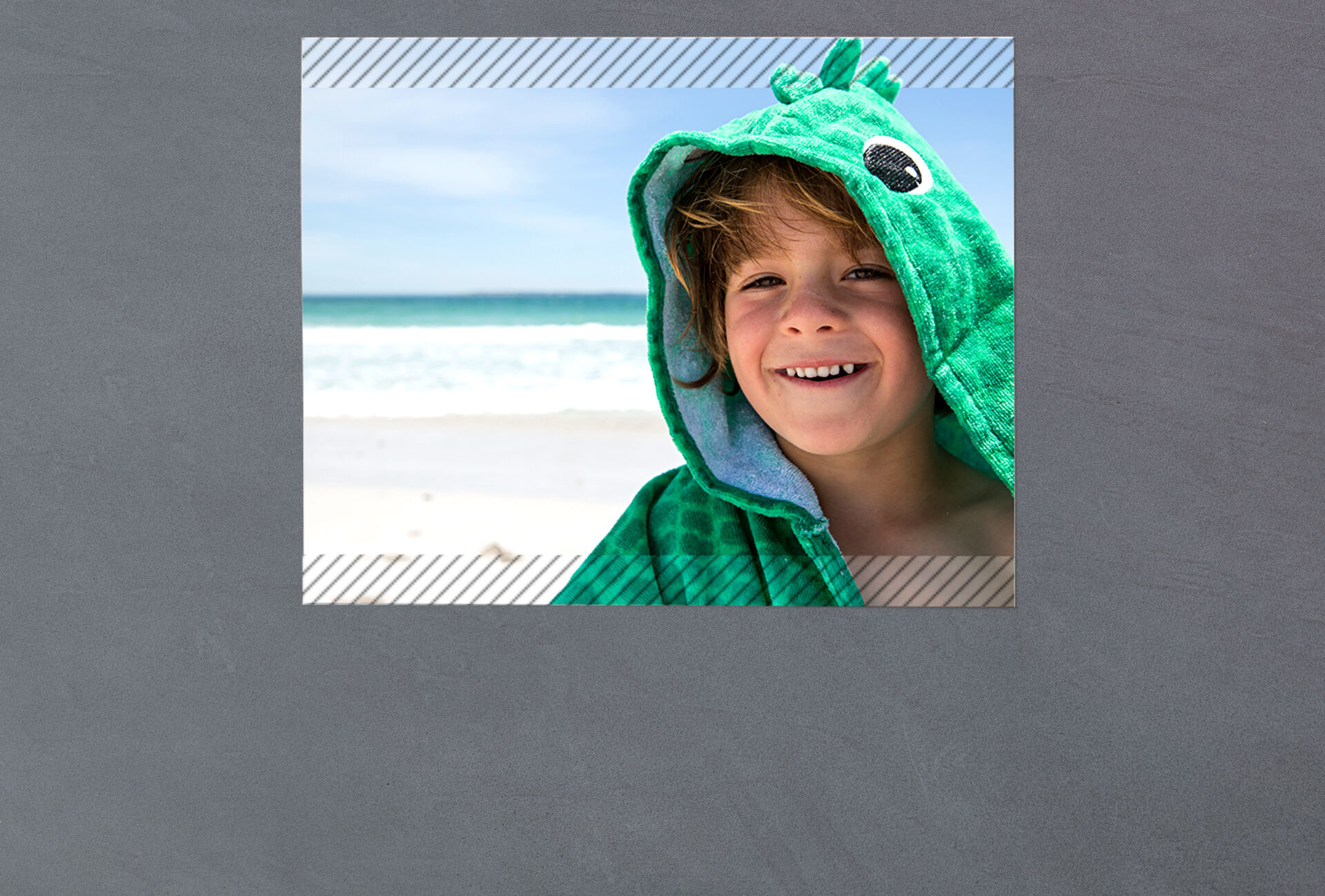 Ein Kind in einem grünen Tierhandtuch steht am Strand und genießt den Tag.