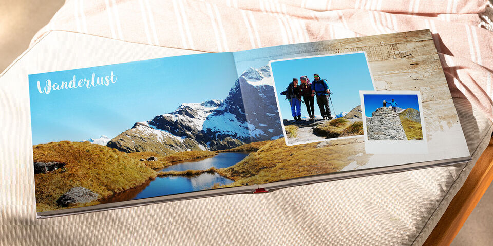 Ein aufgeschlagenes Fotobuch mit Bildern von Wanderungen und der Aufschrift "Wanderlust".