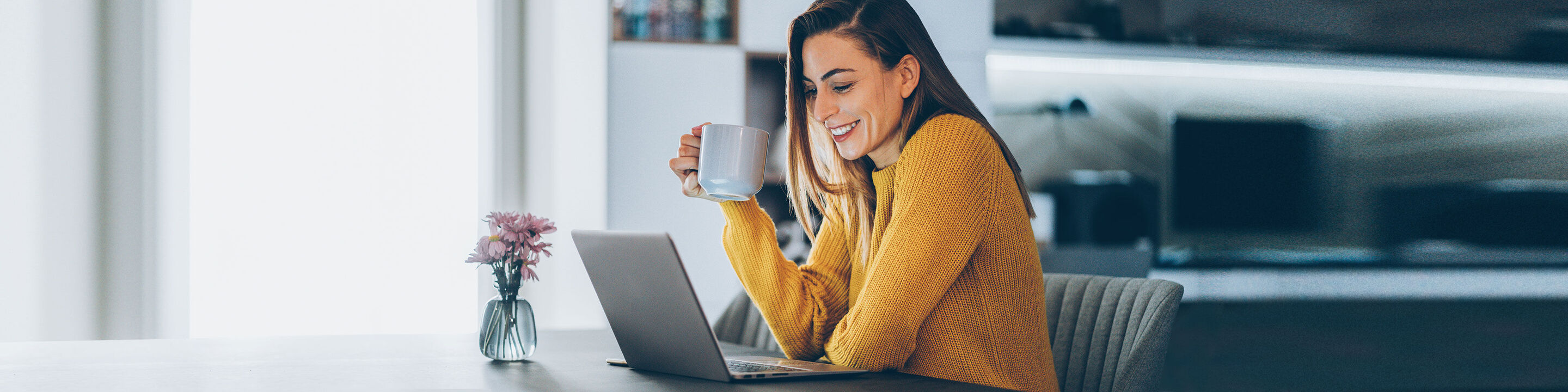 Eine Person in gelbem Pullover genießt eine Tasse Kaffee beim Arbeiten am Laptop