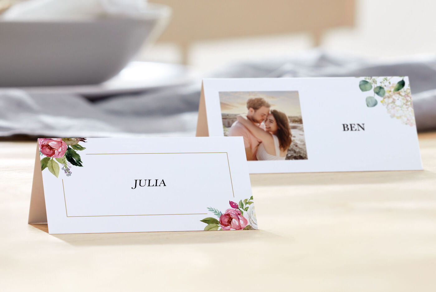 Zwei Tischkarten mit den Namen Julia und Ben, umrahmt von blühenden Blumen und einem Foto.