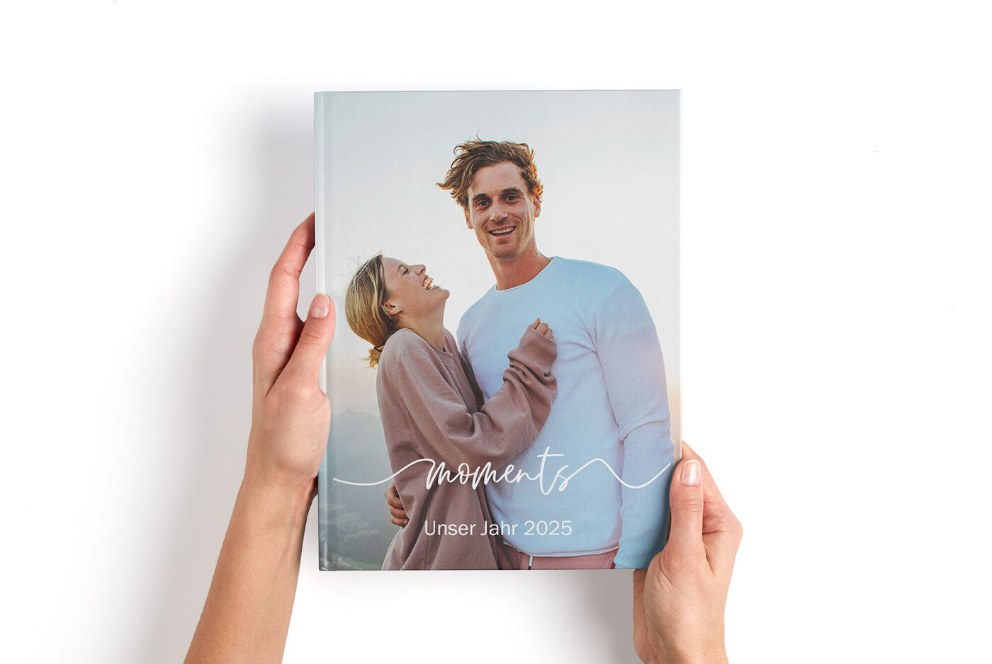 Zwei Menschen halten ein CEWE FOTOBUCH mit dem Titel moments Unser Jahr in den Händen