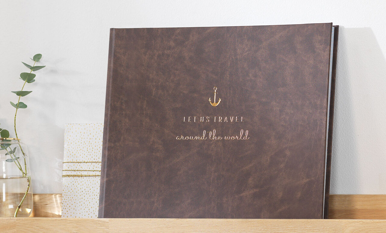 Ein hochwertiges Fotobuch mit dem Titel 'Jeremy's Travel around the world' in braunem Lederdesign auf einem Regal.