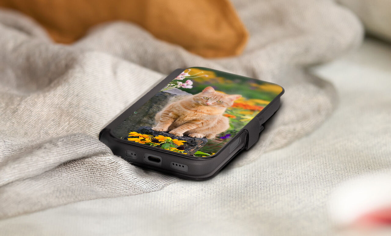 Smartphone Hülle liegt auf einer Decke und zeigt ein persönliches Foto einer Katze zwischen bunten Blumen