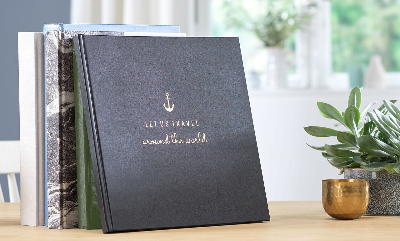 Ein stilvolles CEWE Fotobuch mit einem maritimen Design liegt auf einem Tisch, umgeben von Pflanzen und einer harmonischen Umgebung.