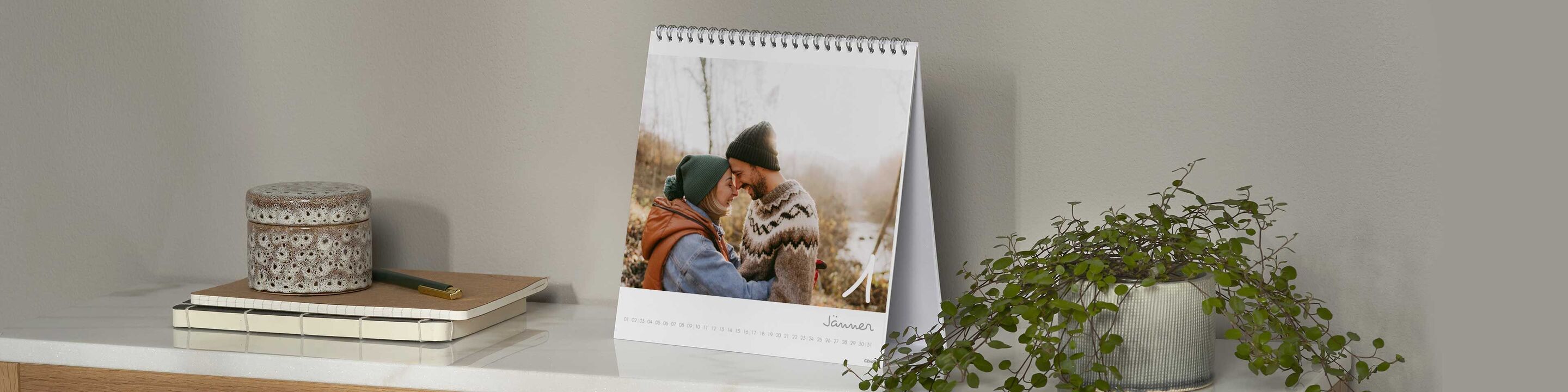 Ein auf einem Tisch stehender CEWE Fotokalender zeigt ein liebevolles Bild von zwei Personen, die sich umarmen und lächeln.