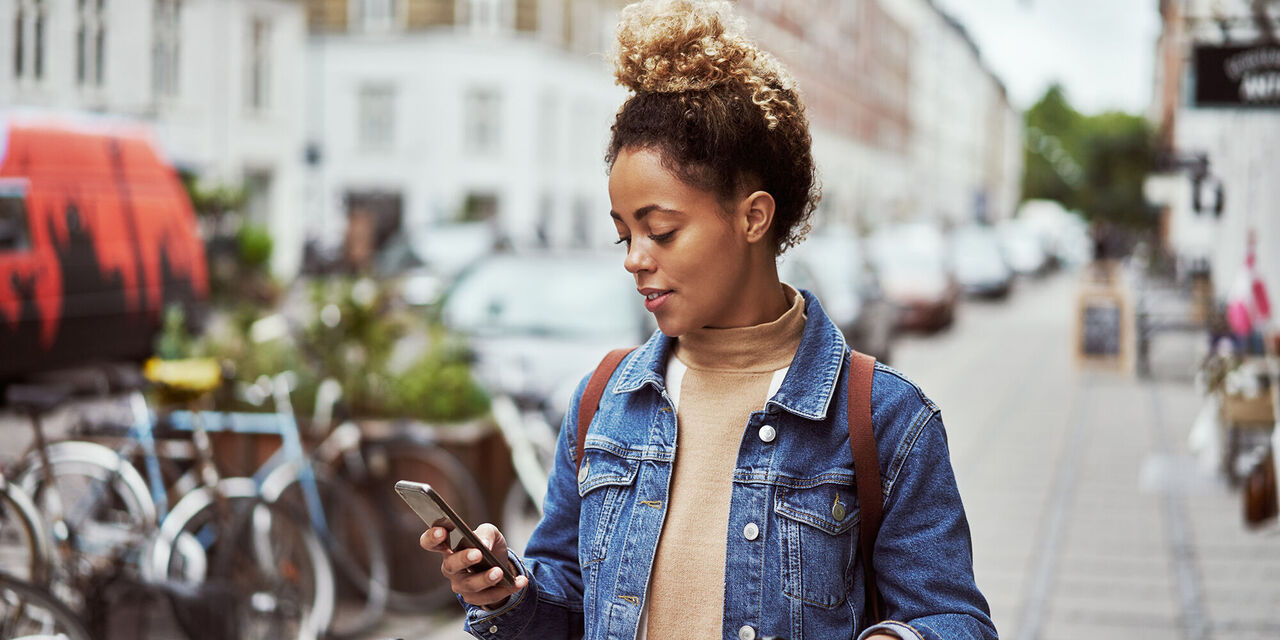 Junge Frau in einer Stadt mit einem Smartphone in der Hand, lächelt und genießt den Moment.