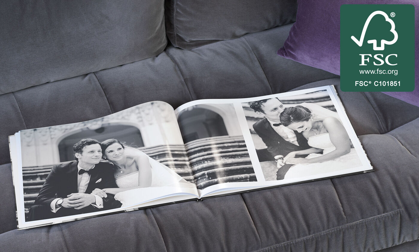 Ein geöffnetes CEWE FOTOBUCH liegt auf einem grauen Sofa und zeigt eine romantische schwarz-weiße Fotodoppelseite einer Hochzeit.
