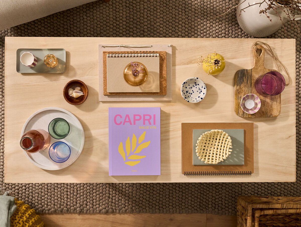 Auf einem Couchtisch liegt ein CEWE FOTOBUCH. Das Cover ist pink und mit dem Schriftzug „Capri“ gestaltet.