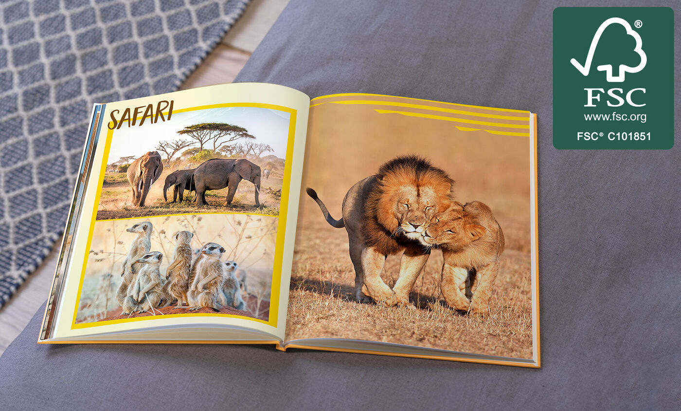 Ein aufgeschlagenes Fotobuch mit Safari-Thema. Links sind Elefanten und Erdmännchen abgebildet, rechts zwei spielende Löwen.