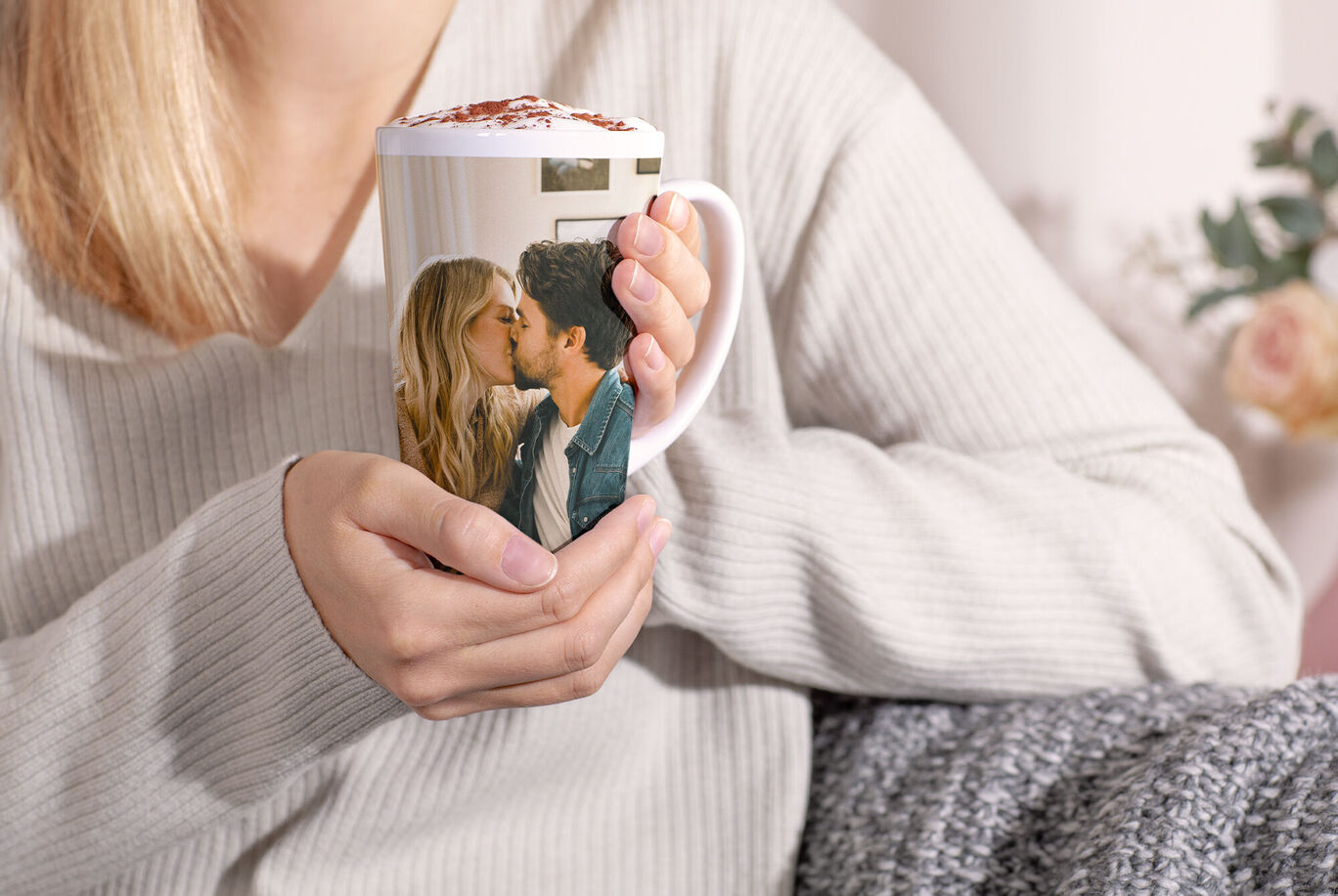 Eine Person hält eine Tasse, die ein Liebespaar zeigt, in einer gemütlichen Umgebung
