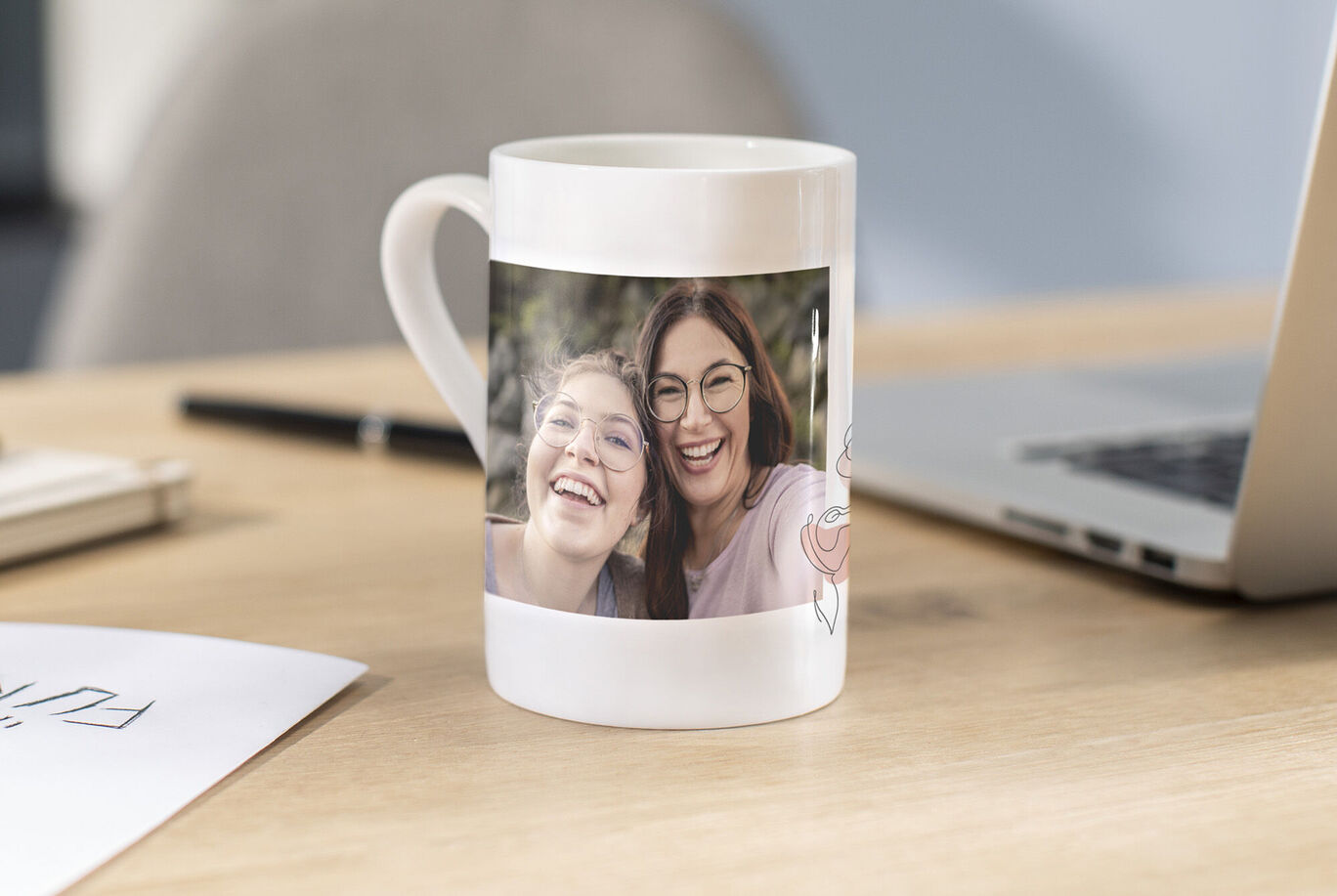 Eine wunderschöne Tasse mit einem persönlichen Foto von zwei glücklichen Menschen, die gemeinsam lachen, auf einem Holztisch. Im Hintergrund ist ein Laptop zu sehen.