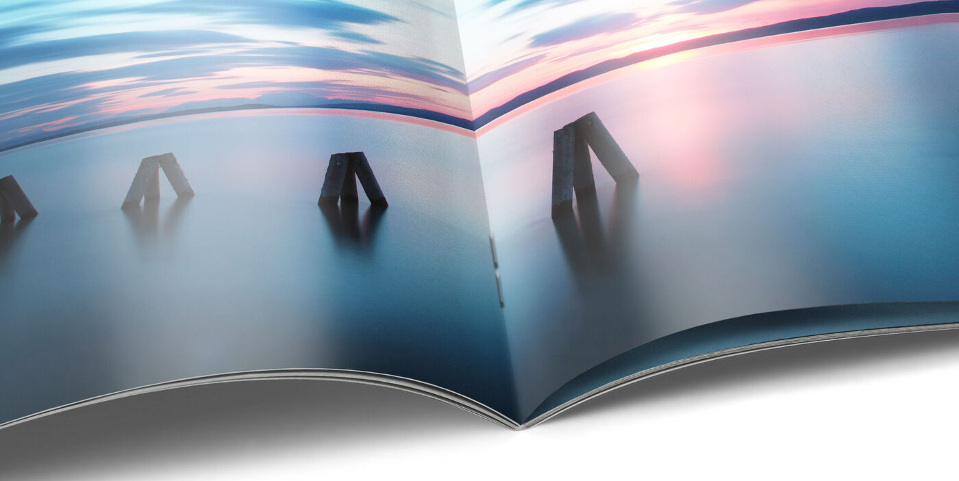Aufgeschlagenes CEWE FOTOBUCH mit fotografischer Land- und Seelandschaft auf einer Seite