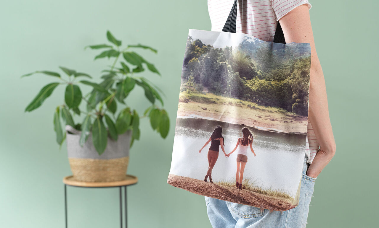 Zwei Frauen halten Händchen am Strand, auf ihrer Tasche ist ein zauberhaftes Landschaftsbild zu sehen