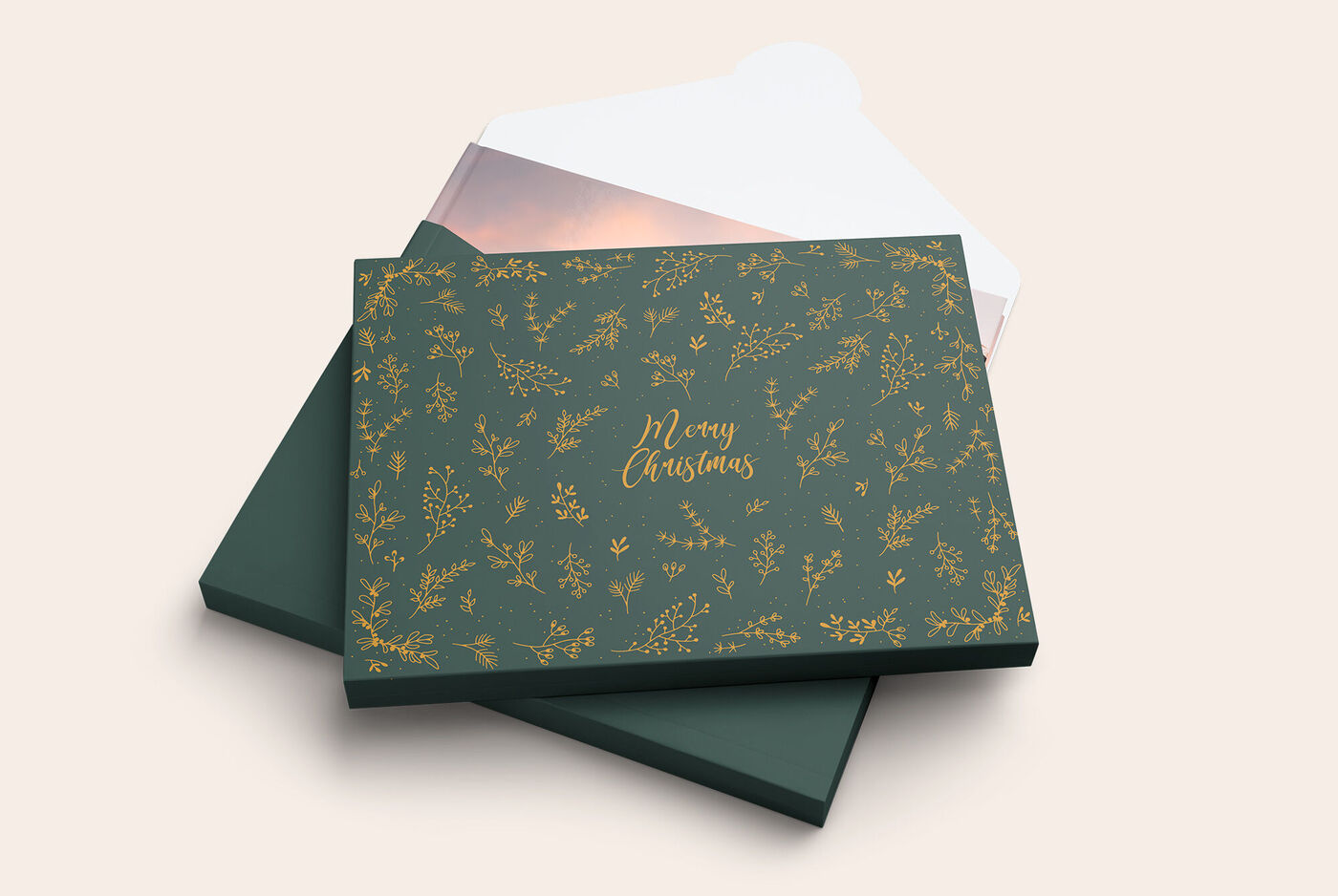 Ein wunderschönes CEWE FOTOBUCH mit einem eleganten grünen Cover, dekoriert mit goldenen Pflanzenmotiven und der Aufschrift „Merry Christmas“. Es liegt auf einem weißen Hintergrund.