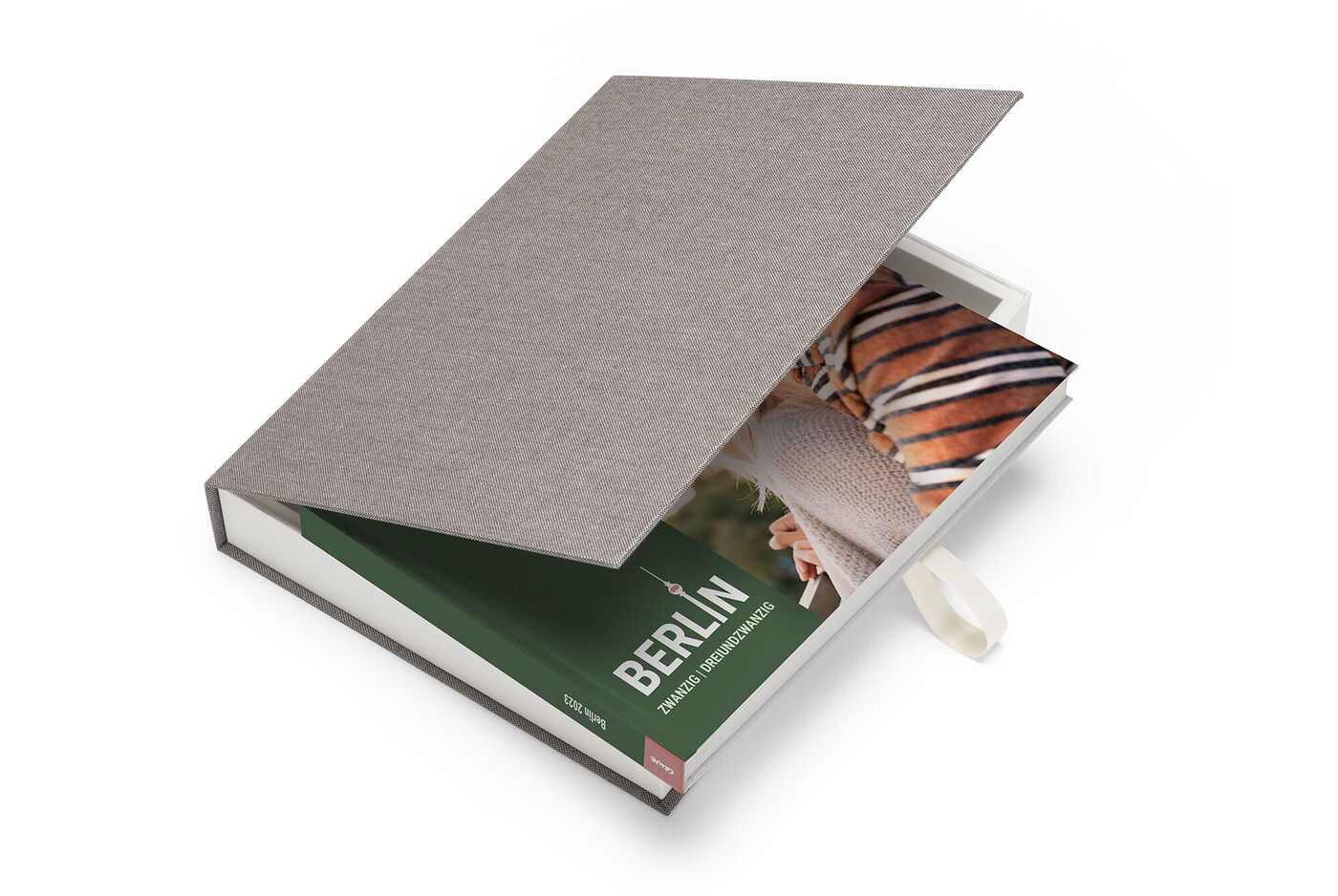 Ein geöffnetes CEWE FOTOBUCH mit einem Bild von Berlin auf der Innenseite und einem grauen Stoffumschlag.