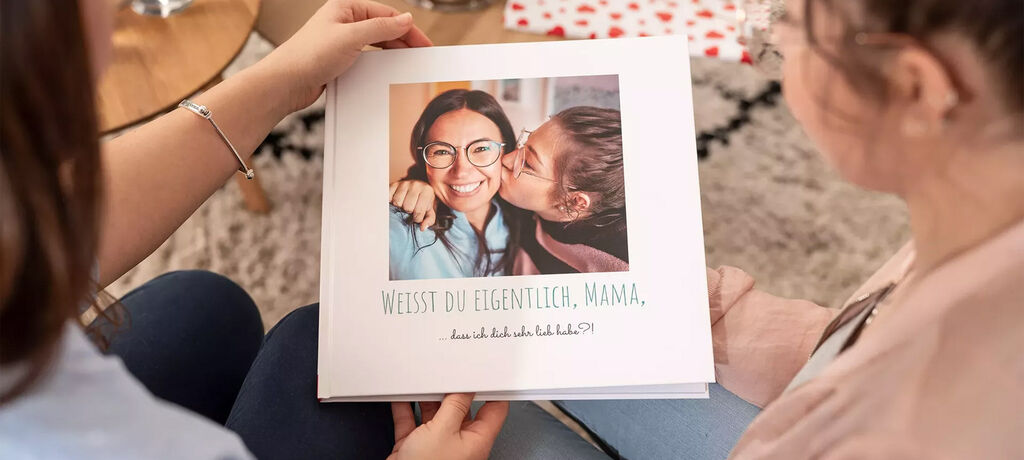 Zwei Personen halten ein CEWE FOTOBUCH mit herzlichem Cover in ihren Händen