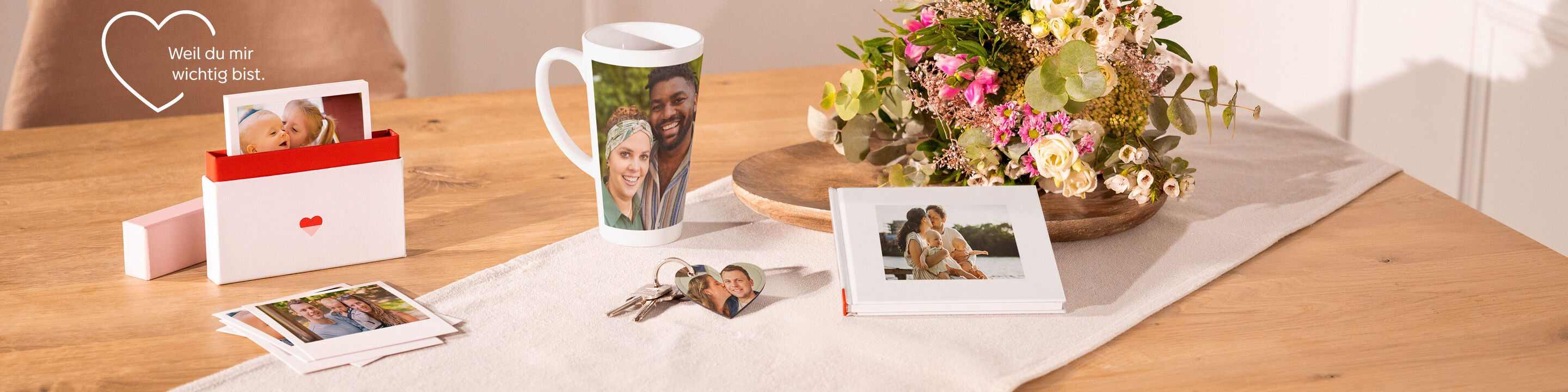 Ein liebevoll gestalteter Tisch mit persönlichen Erinnerungen. Darauf sind Fotos, eine Tasse mit Bildern, ein Erinnerungsalbum und eine Blume.