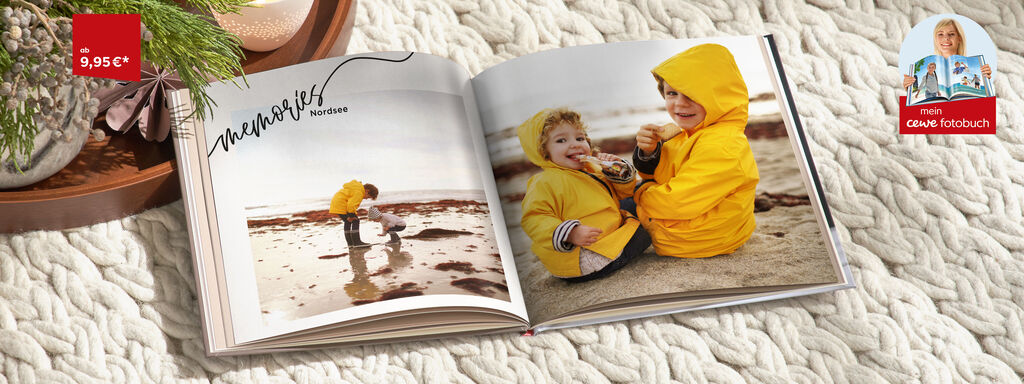 Zwei Kinder in gelben Regenjacken betrachten ein Fotoalbum am Strand.