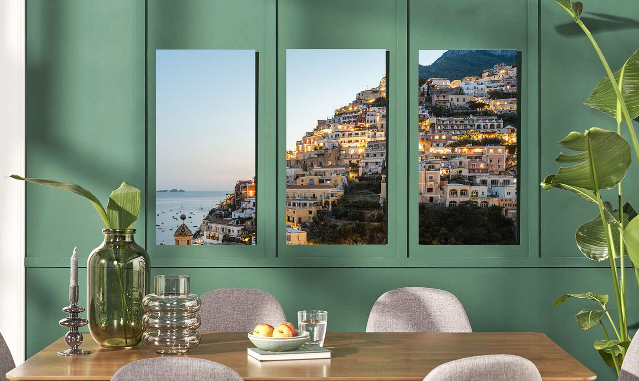 Drei Bilder von Positano an einer Wand in einem modernen Raum mit einer eleganten Tischdeko