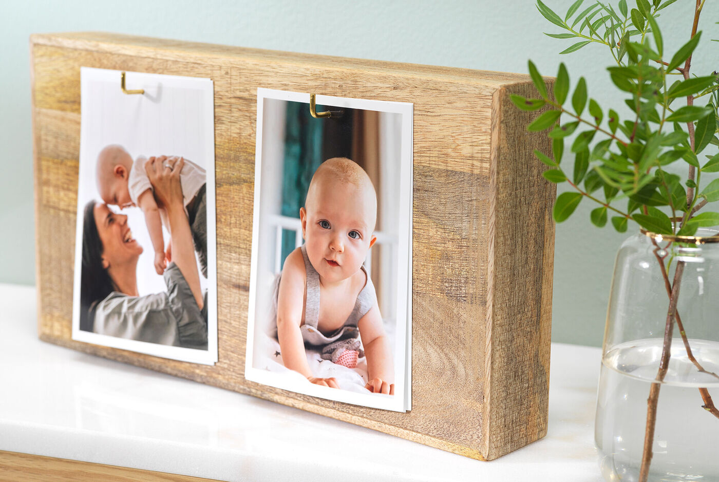 Zwei Fotos auf einem Holzdisplay, eines zeigt eine Mutter mit ihrem Baby, das andere ein Baby in einem gemütlichen Raum