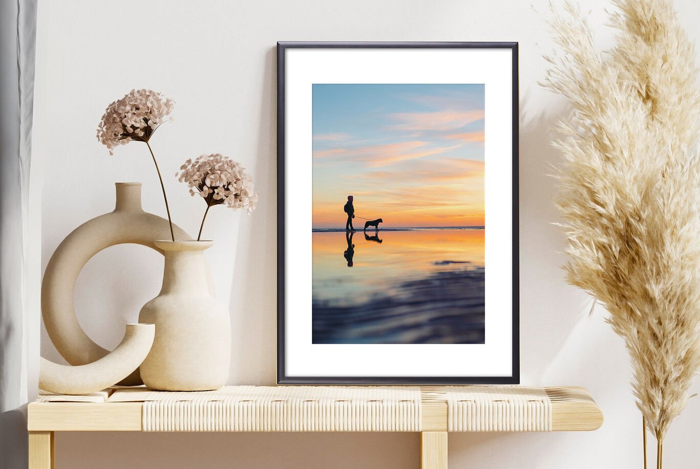 Eine Frau mit ihrem Hund steht am Strand. Der Himmel hat schöne Farben beim Sonnenuntergang.