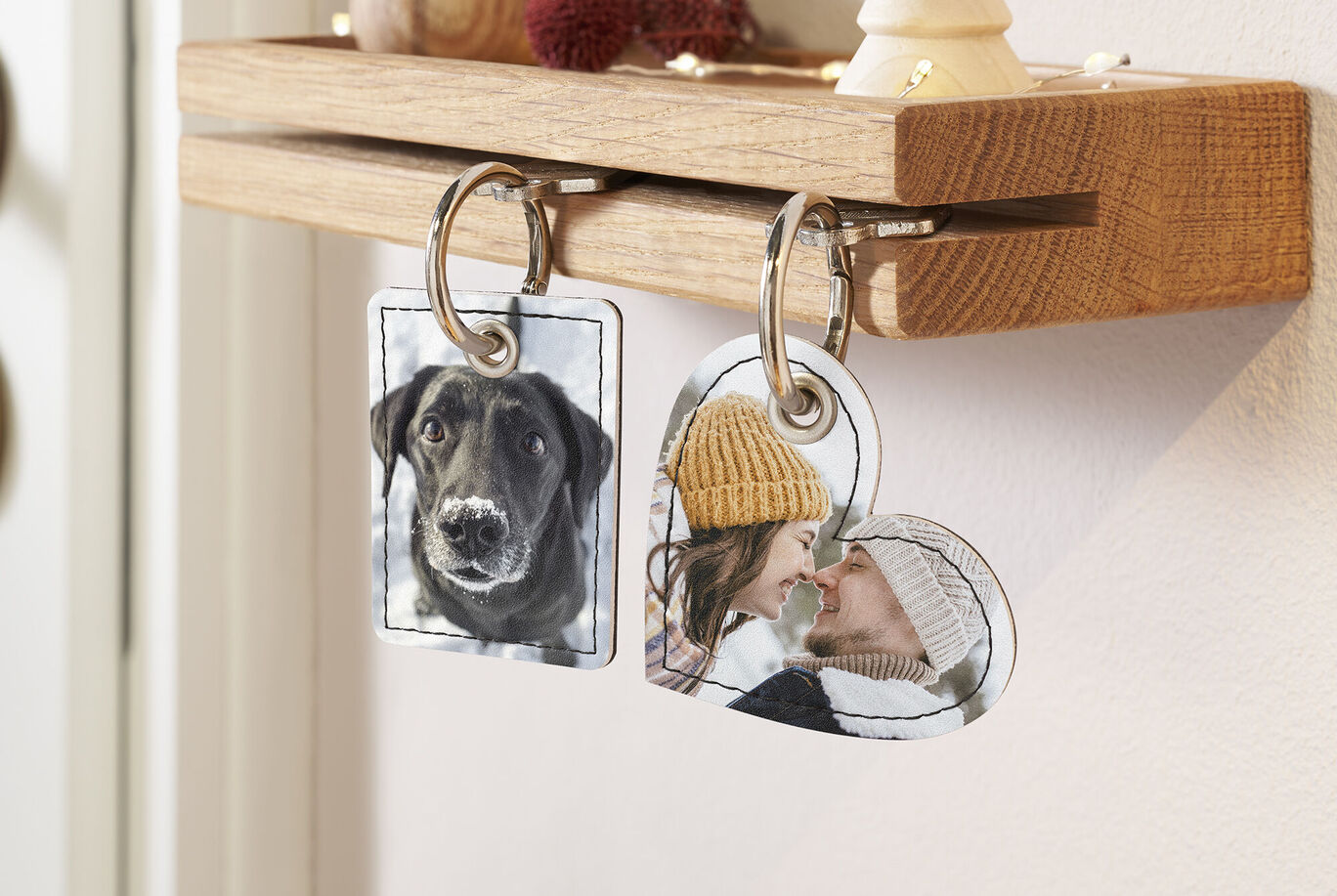 Zwei personalisierte Schlüsselanhänger hängen an einem Holzbrett. Einer zeigt einen Hund, der andere eine Person mit einer Mütze.