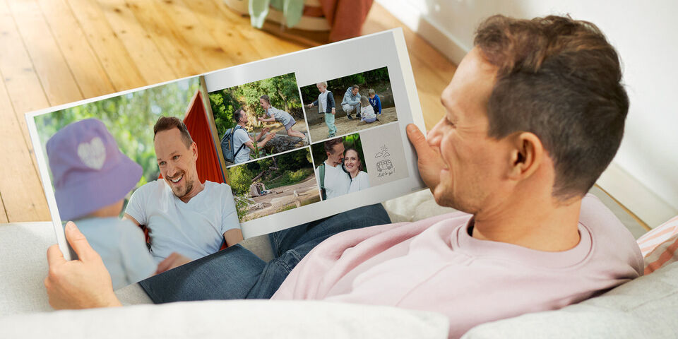 Ein Mann liest ein CEWE FOTOBUCH mit Erinnerungen an fröhliche Momente im Freien.