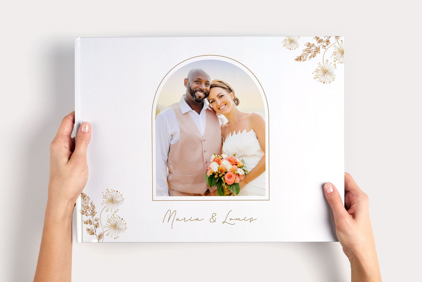 Zwei Hände halten Hochzeits- CEWE FOTOBUCH XXL Panorama mit Paarfoto in Bogenrahmen und Schriftzug "Maren & Lucas"